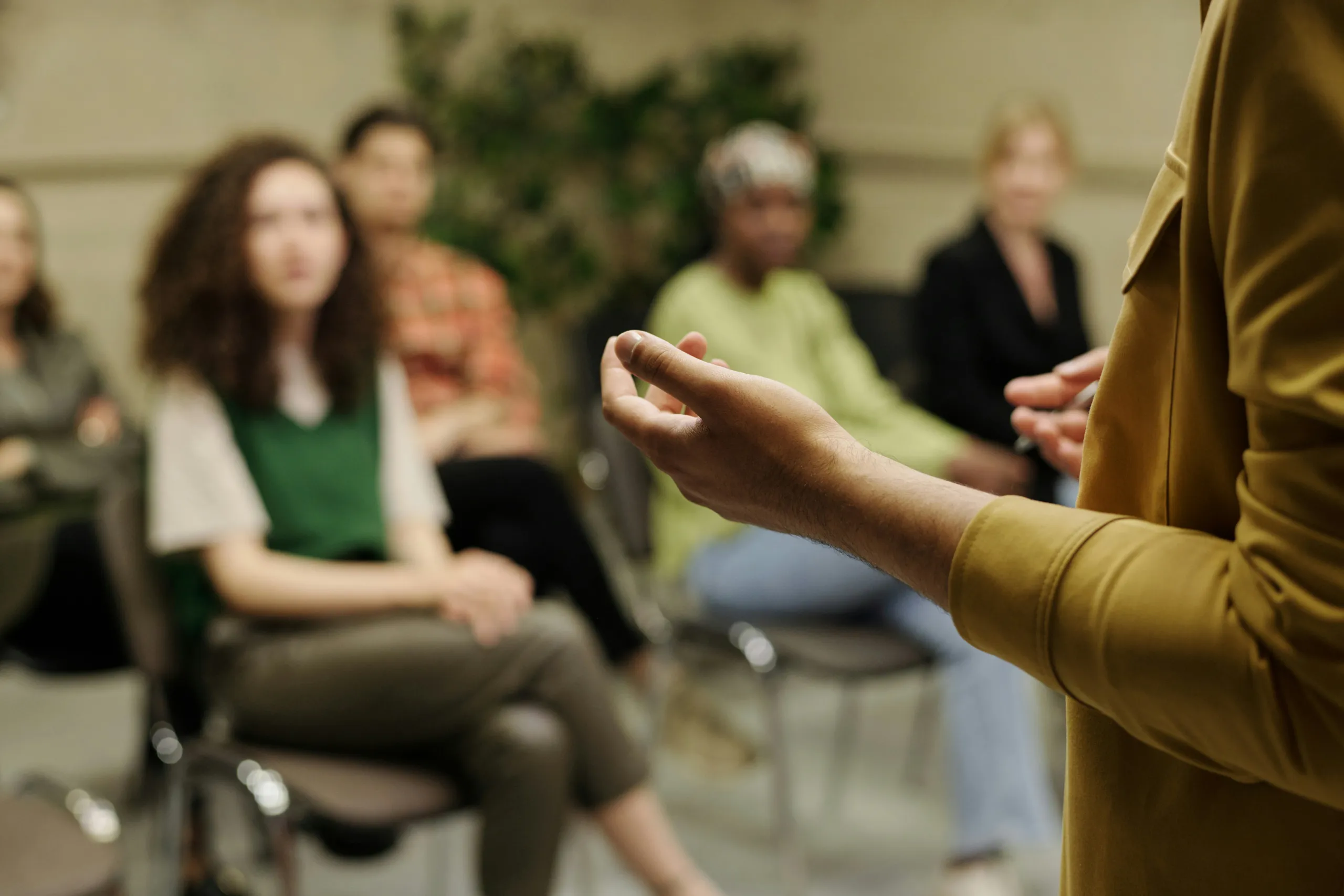 A speaker gestures to a circle of seated people listening